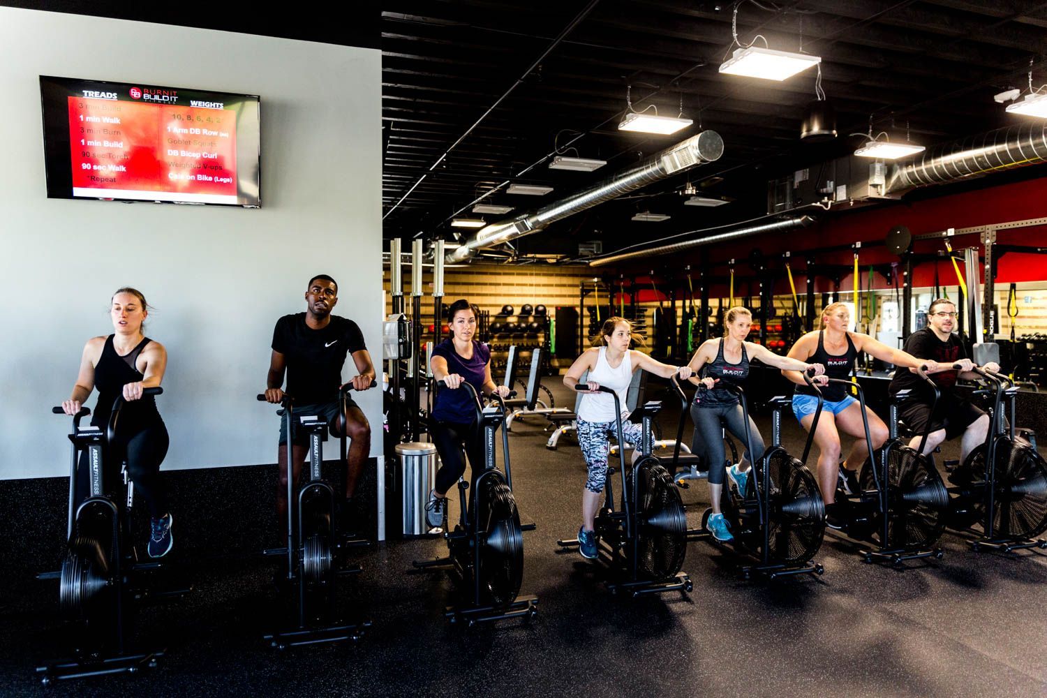 People on stationary bikes in a gym, with a TV on the wall.