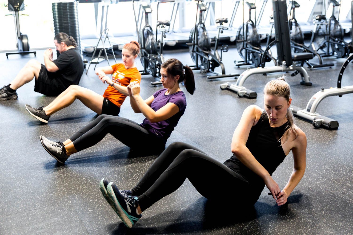 Four people doing Russian twists on gym floor.