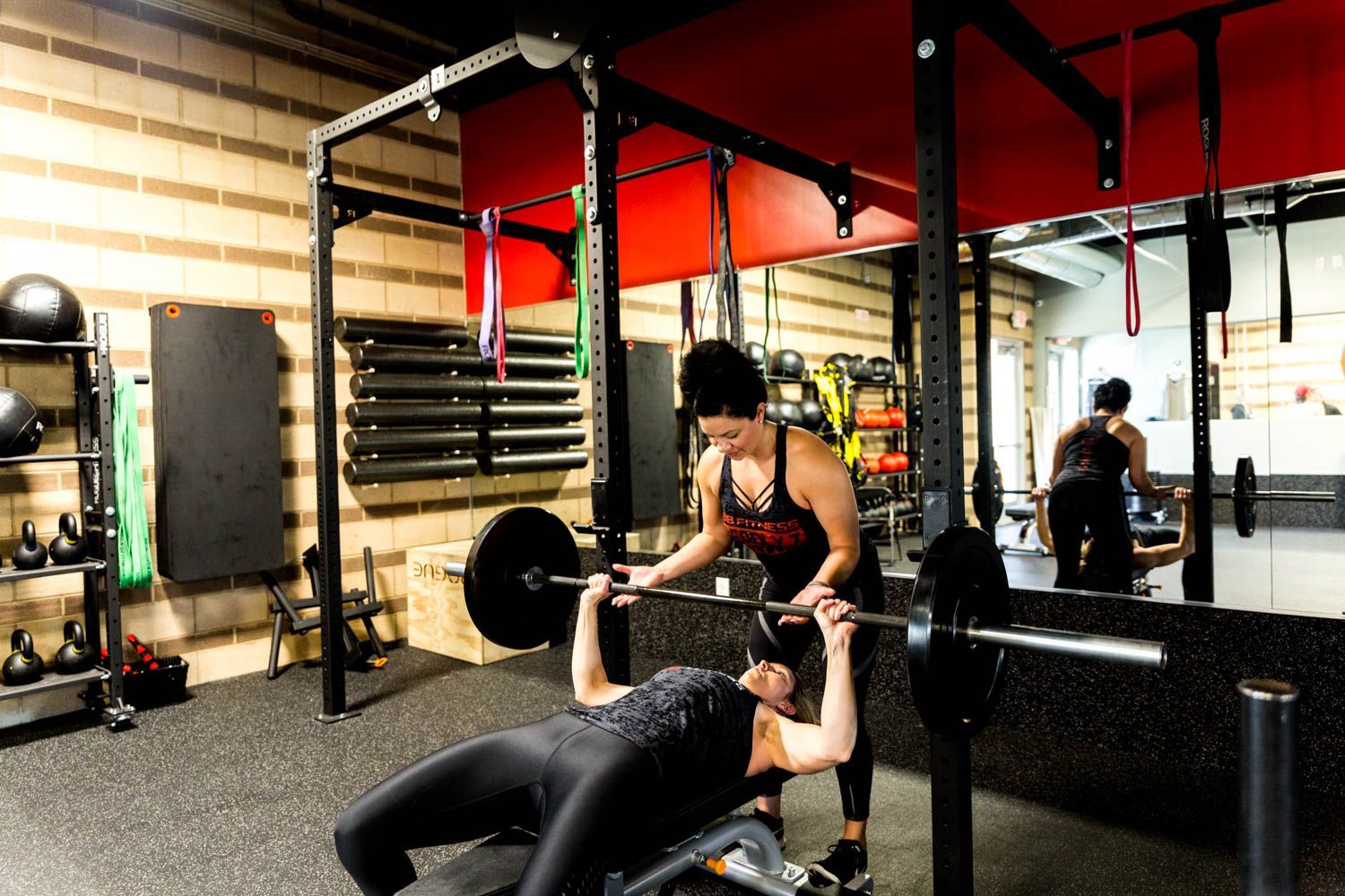 Woman bench pressing with spotter in a gym, black barbell and equipment.