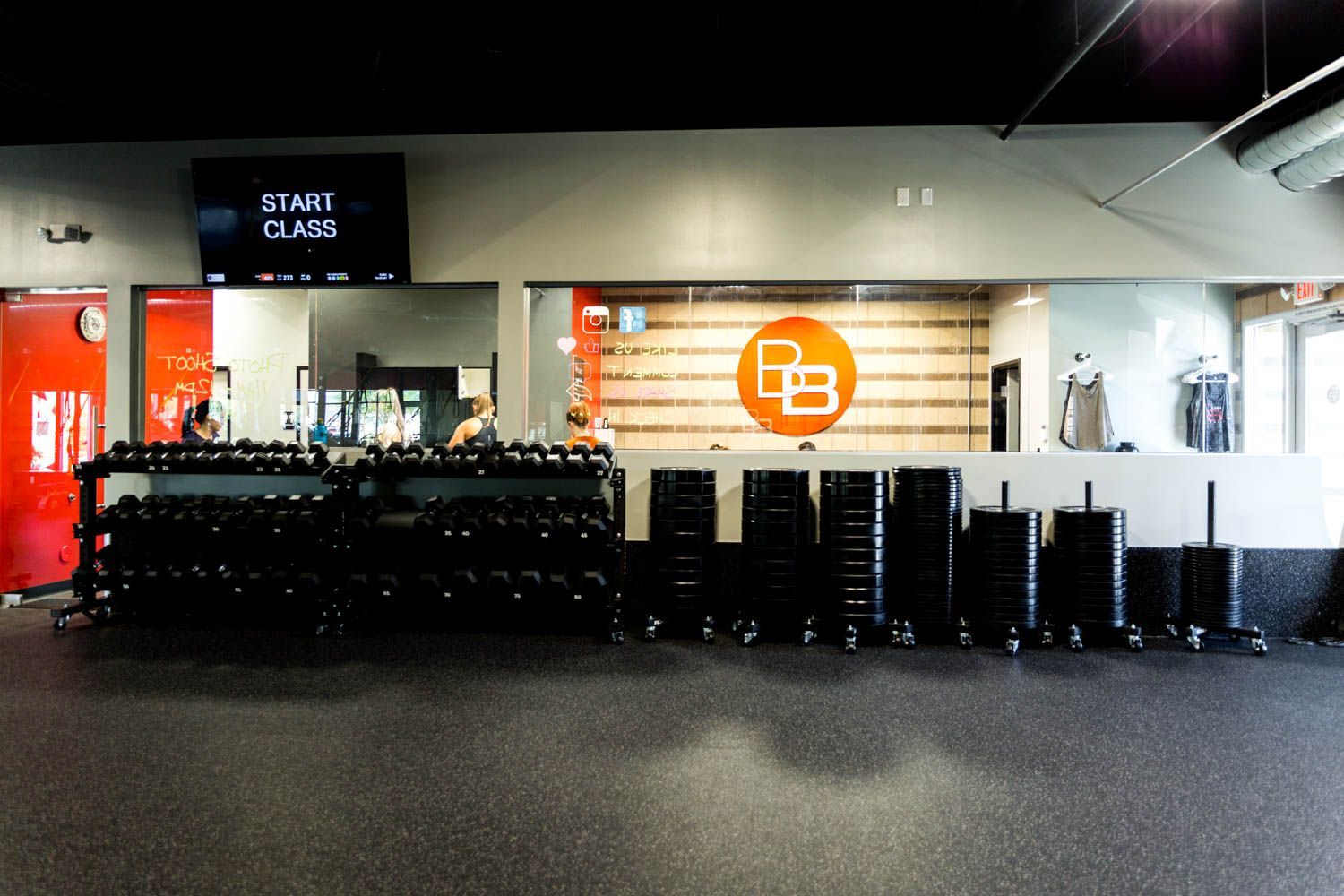 Weight room with dumbbells, weight plates, and logo on wall.