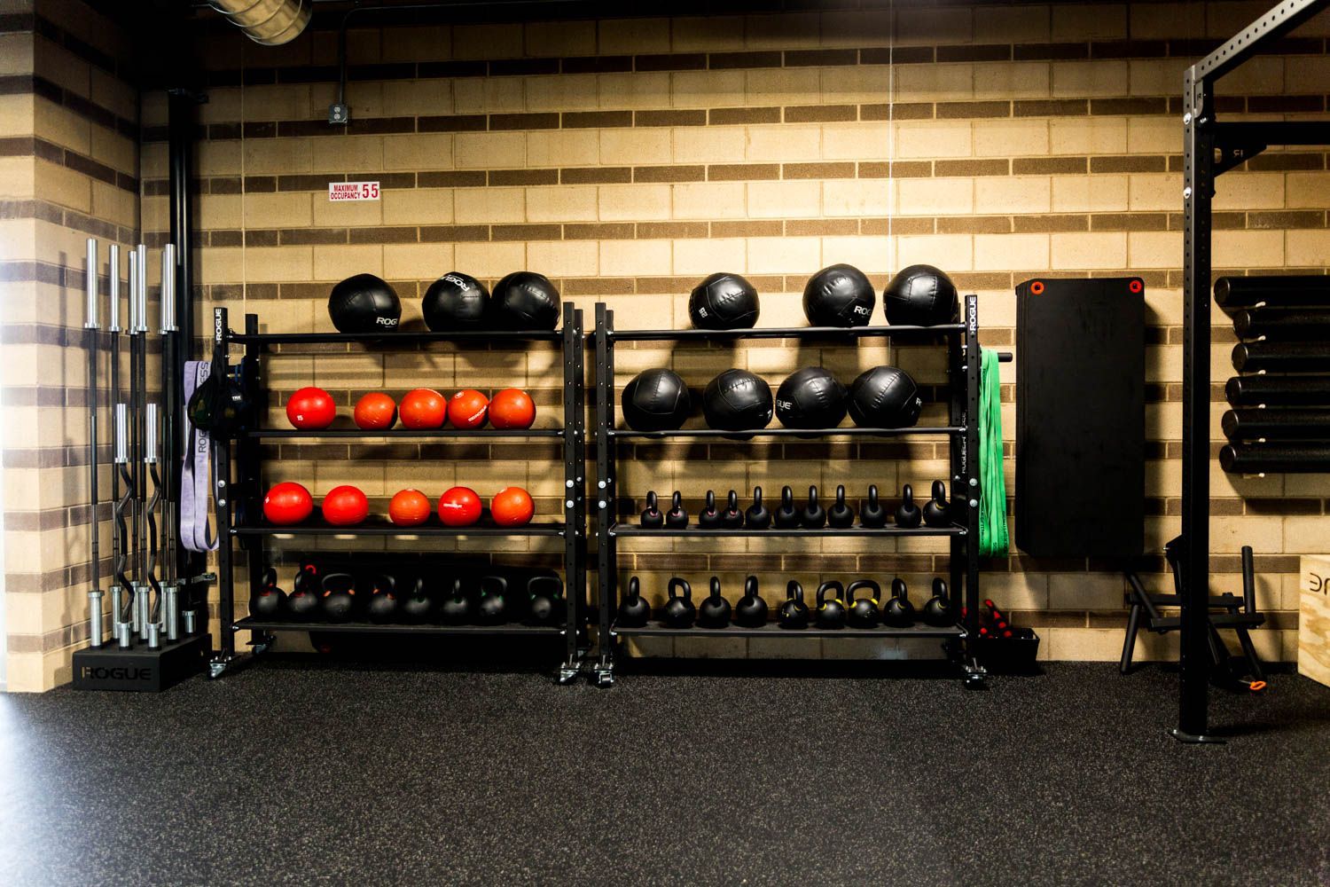 Gym equipment storage rack against a brick wall. Contains medicine balls, kettlebells, and barbell racks.