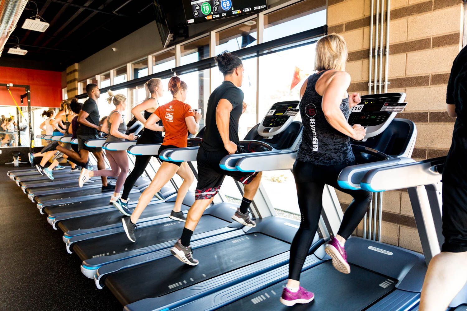 People running on treadmills in a gym with windows and workout equipment.