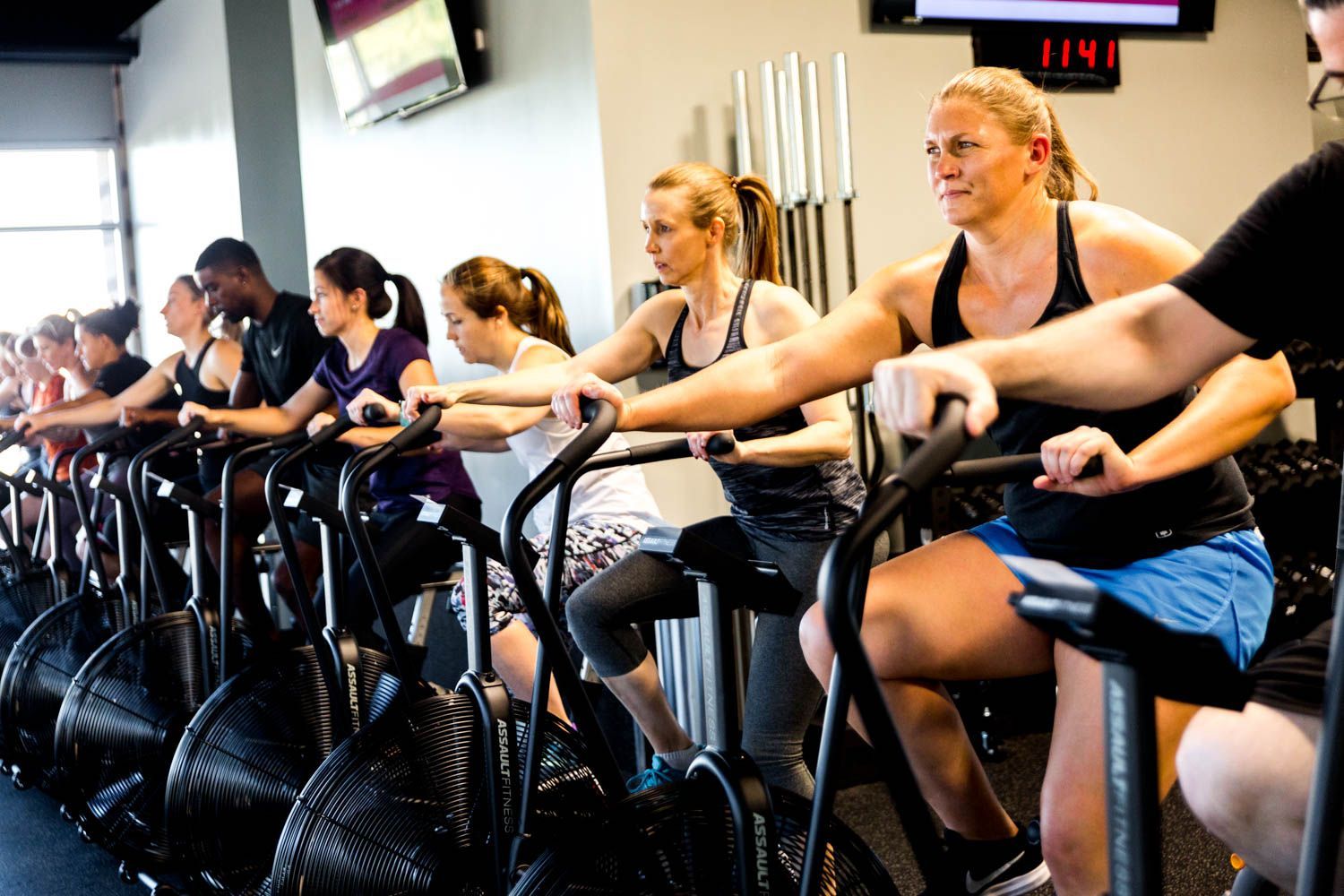 People exercising on air bikes in a gym. They are working out intensely.