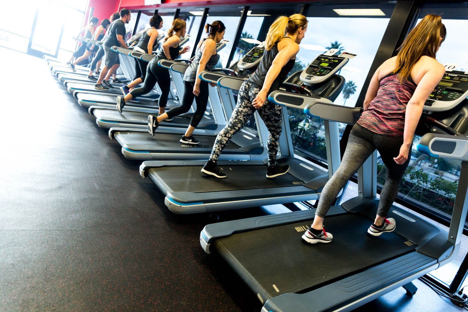 People exercising on treadmills in a gym with large windows.