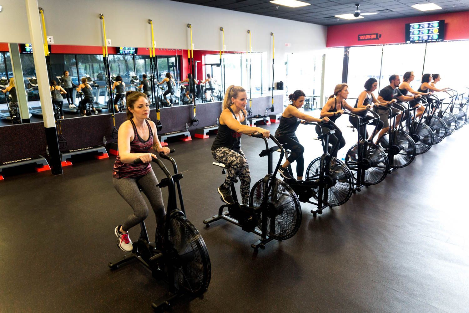 People on stationary bikes in a gym with a red and black color scheme, exercising.