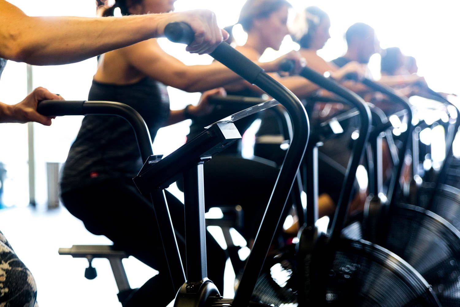 People exercising on stationary bikes in a gym, with focus on the bikes and arms.