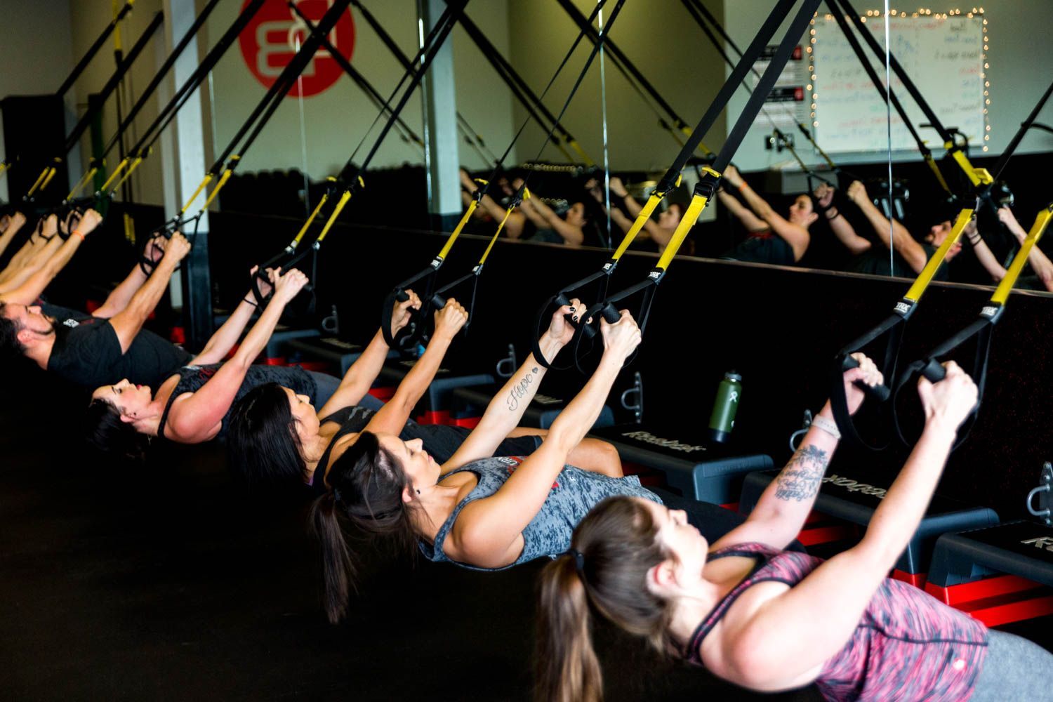 People exercising with suspension straps in a fitness studio. They are pulling on the straps while reclining.