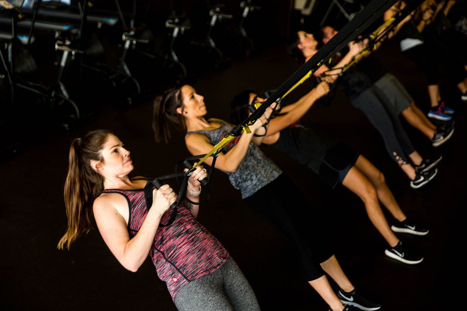 People exercising with TRX straps in a gym, pulling towards themselves.