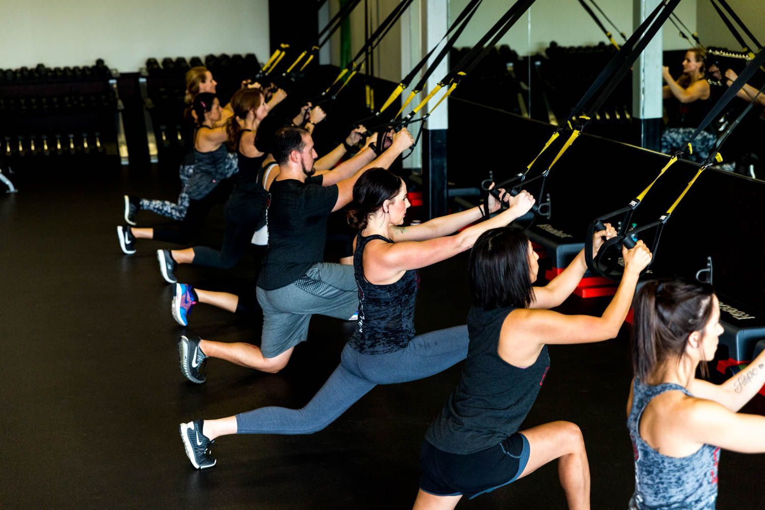 People doing lunges with suspension straps in a gym.