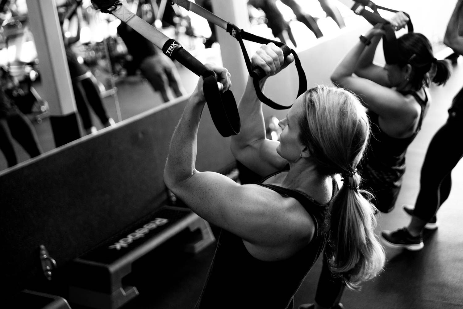 Woman doing TRX suspension training in a gym. Holding straps, she pulls herself up, focusing.