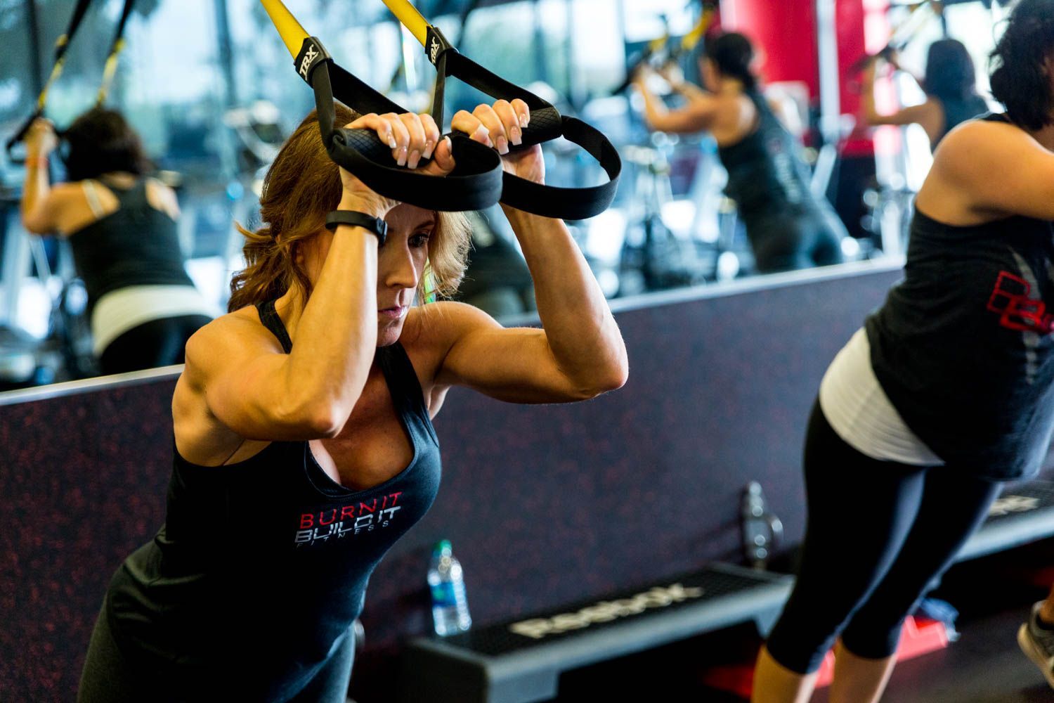 Woman in gym using suspension straps for exercise, other people in background.