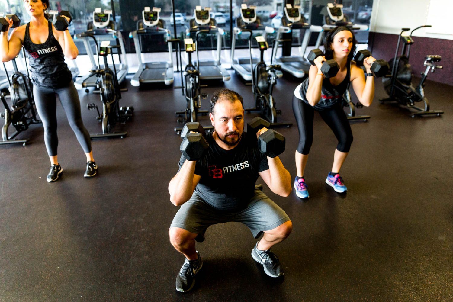 Three people lifting dumbbells in a gym, performing squats.
