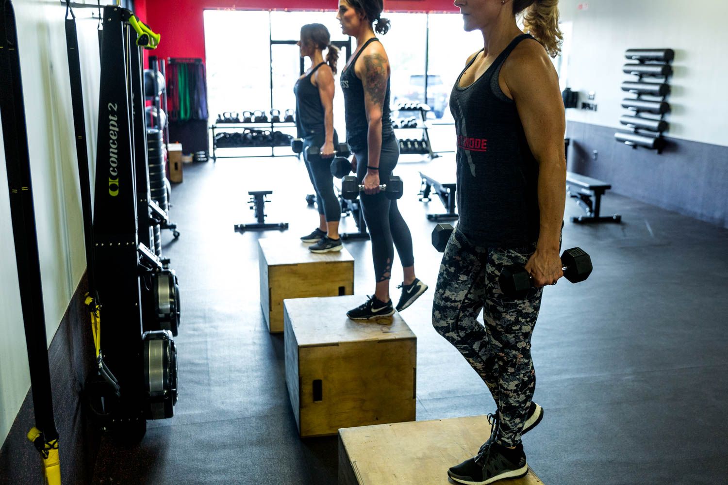 Three women doing step-ups with dumbbells in a gym.
