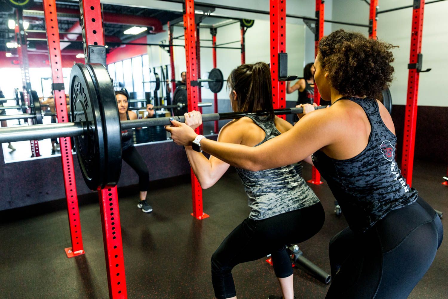 Woman being assisted with squat by another woman at a gym.