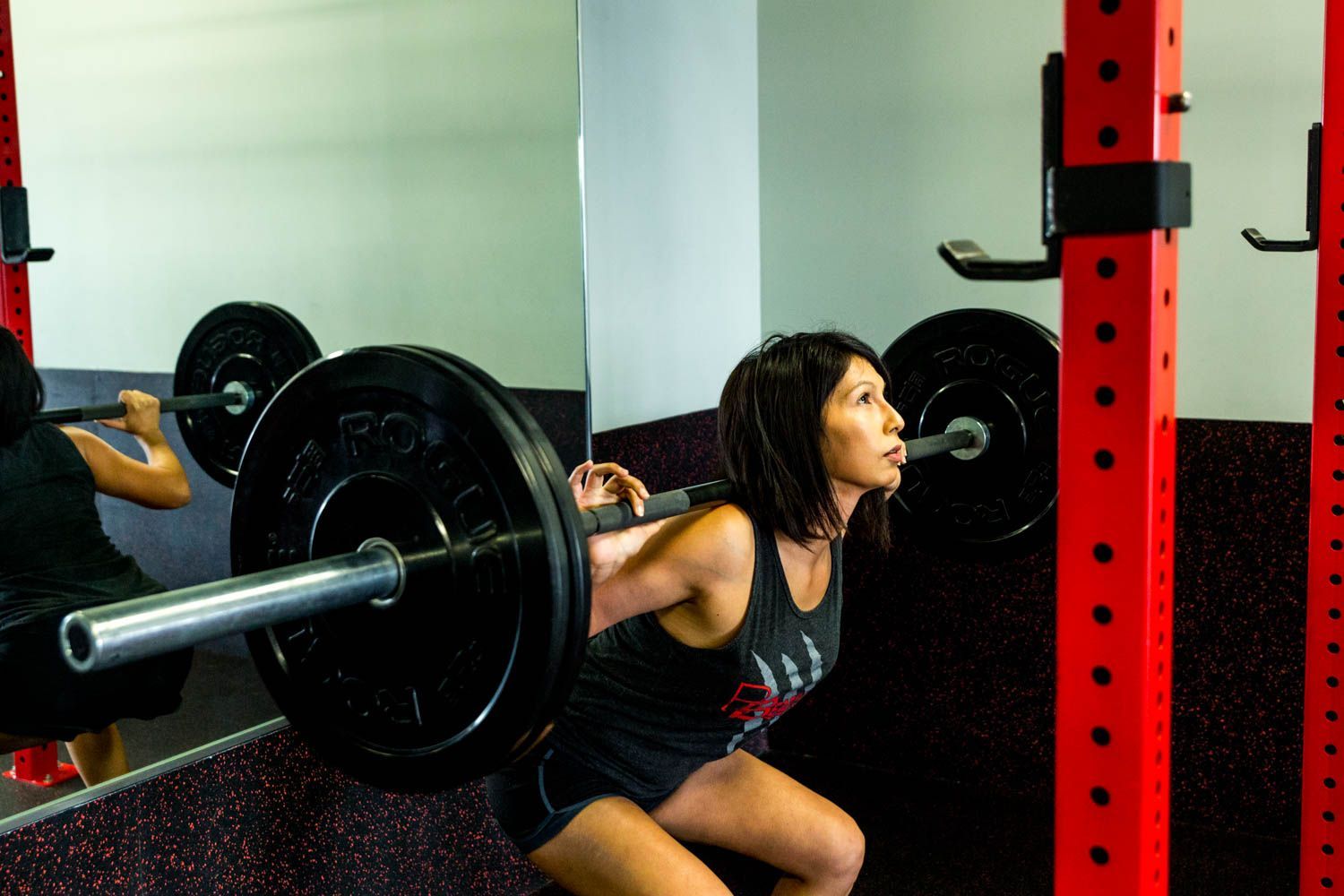 Woman performing a barbell squat in a gym, red rack visible.