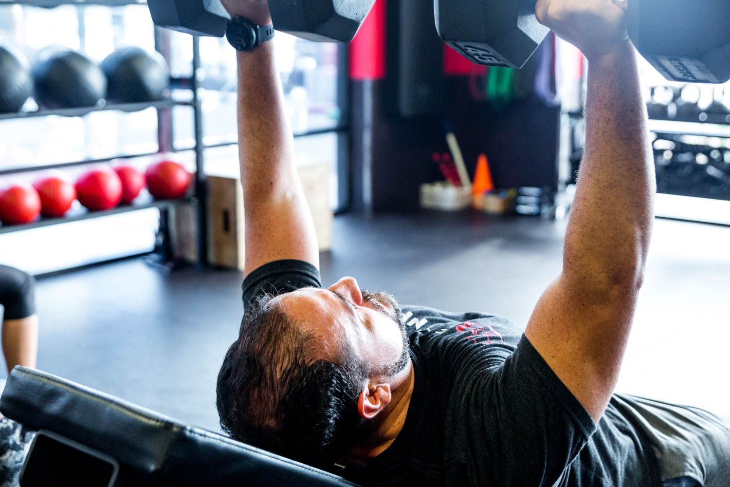 Man lifting dumbbells while lying on a bench in a gym.