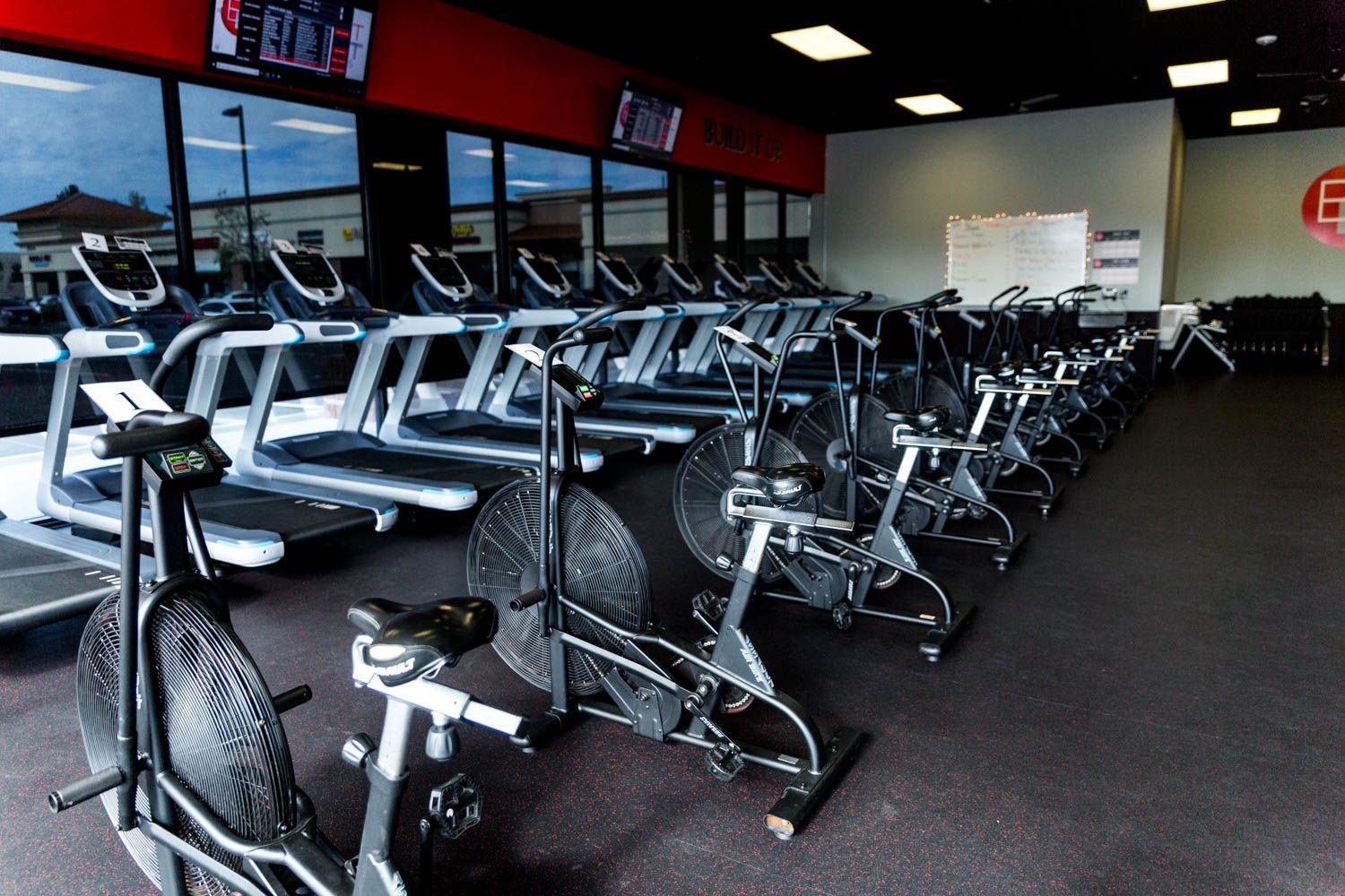 Gym interior with rows of treadmills and stationary bikes, gray and black equipment.