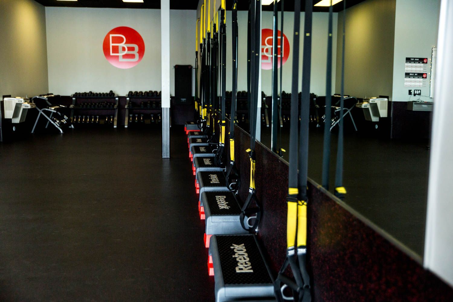 Gym interior with weights, TRX straps, exercise steps, and a large mirror.
