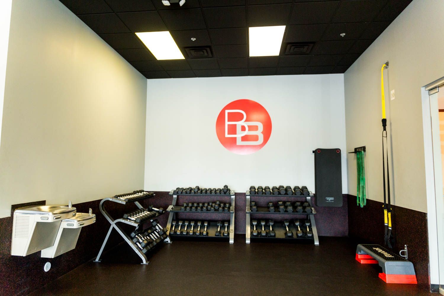 Gym interior with dumbbell racks, a red logo, and fitness equipment.