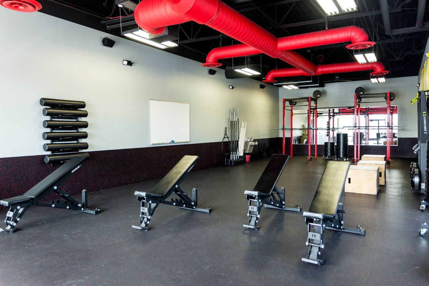 Gym interior with weight benches, red pipes, exercise equipment.