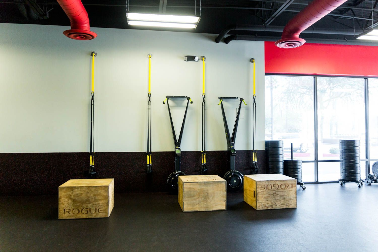 Gym interior with workout equipment: boxes, TRX straps, and handles.