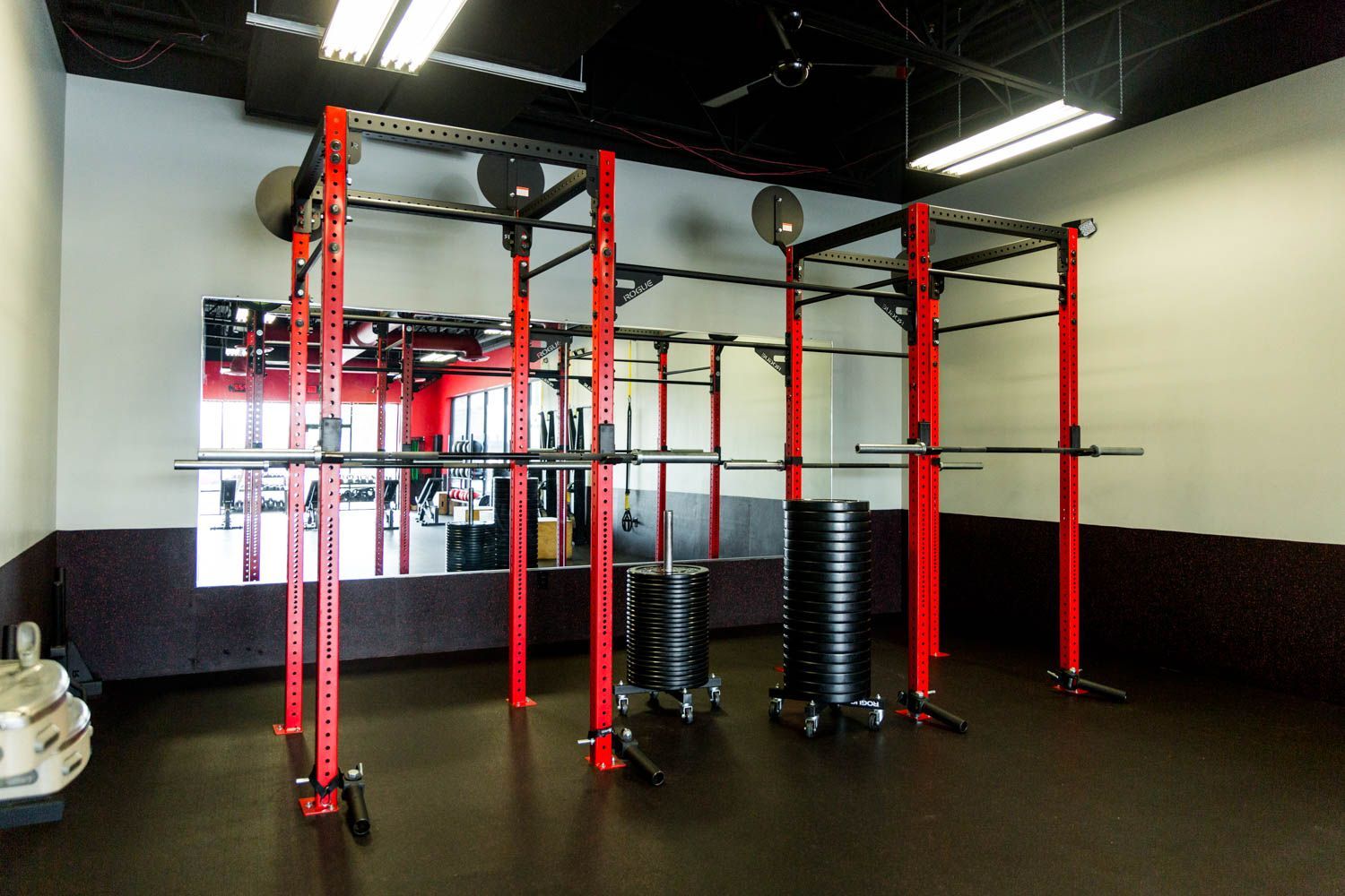 Red and black gym with weightlifting racks, barbells, and weights on a black floor.