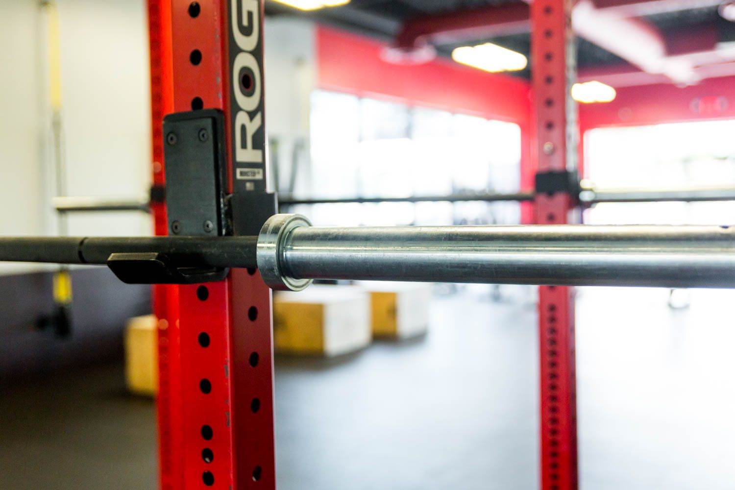 Red weightlifting rack with barbell resting on it, in a gym.
