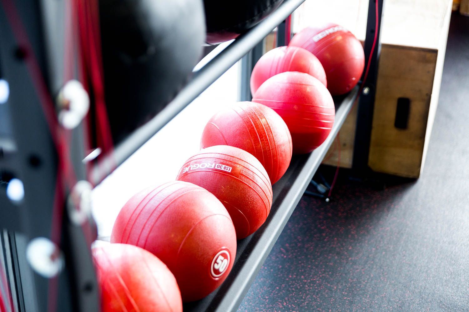 Red medicine balls lined up on a rack in a gym setting.