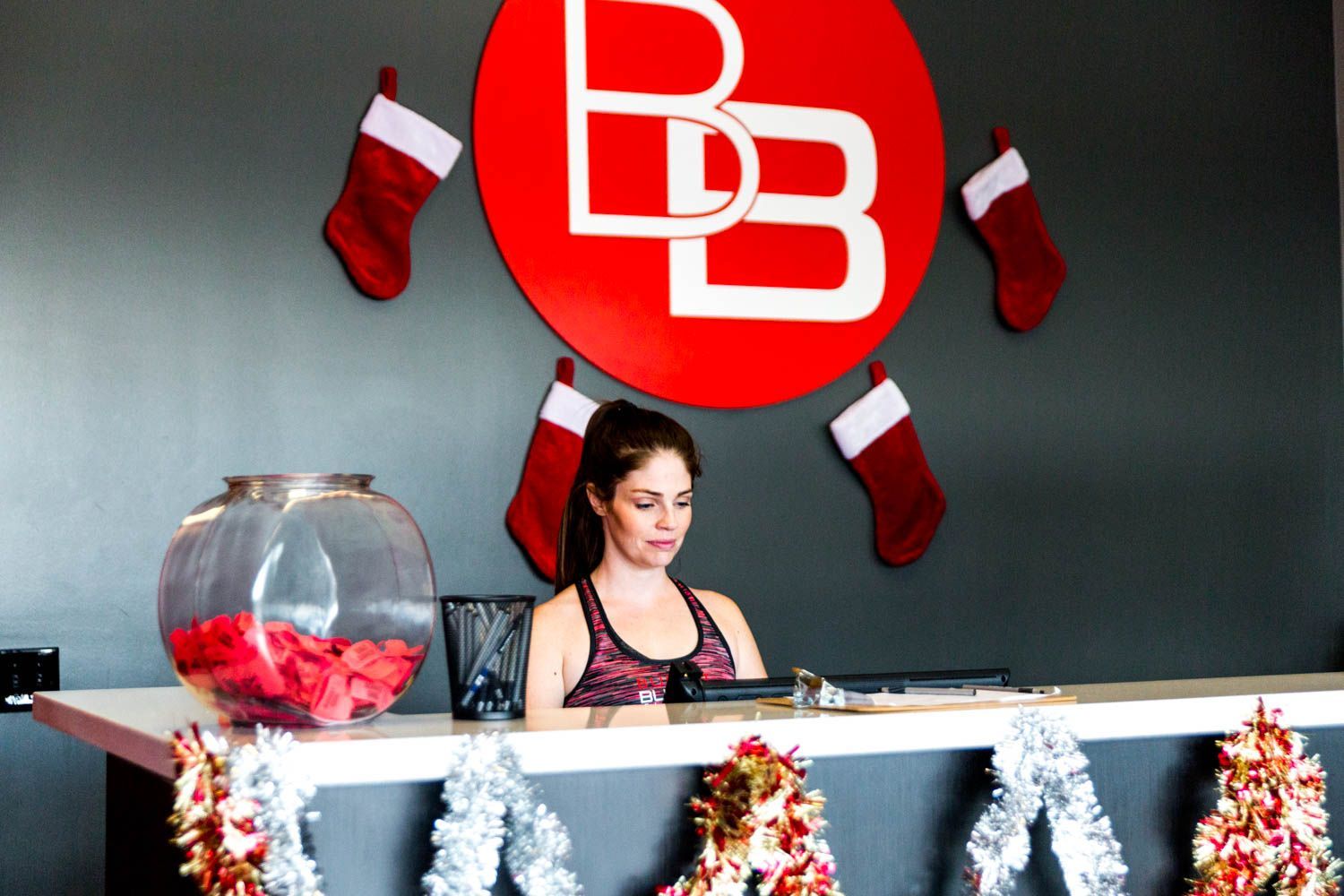 Woman at a gym reception desk, logo above, Christmas decorations, fishbowl, festive.