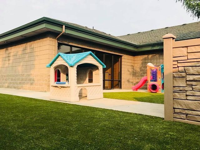 Apartment courtyard with a small blue-roof playhouse and pink slide on a lawn, beside tan brick buildings