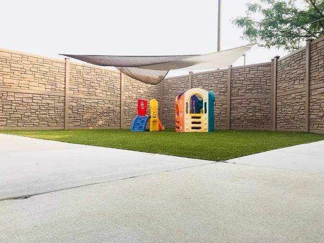 Small playground with colorful play structures on a grassy courtyard beside brick walls and concrete paving