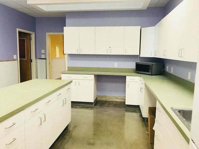 Small kitchen with white cabinets, green countertops, and a gray floor, viewed from the center of the room