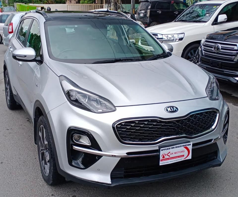 Silver Kia Sportage SUV parked outdoors, with a black roof and other vehicles in the background.