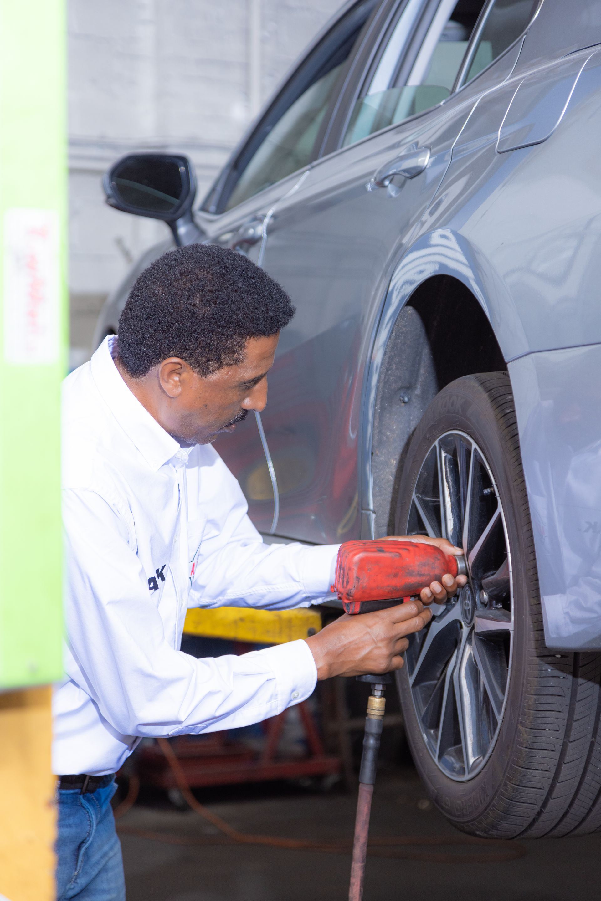 Mechanic using a power tool to remove a car tire in a garage.