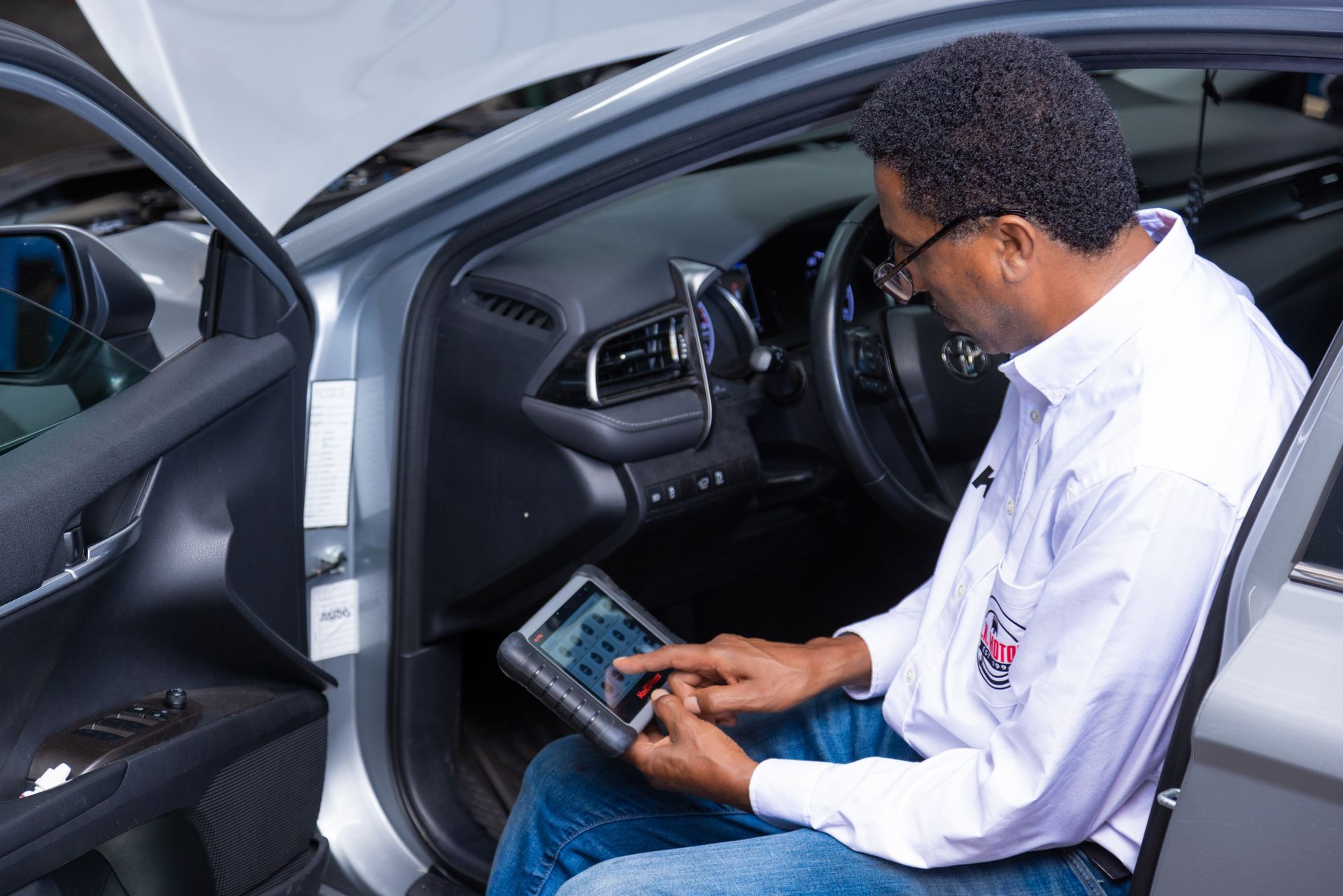 Mechanic using a tablet diagnostic tool inside a car with the hood open.