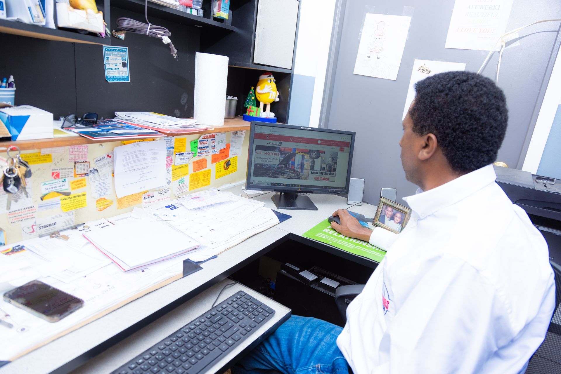 Man in white shirt at desk, looking at computer screen, papers and phone visible.