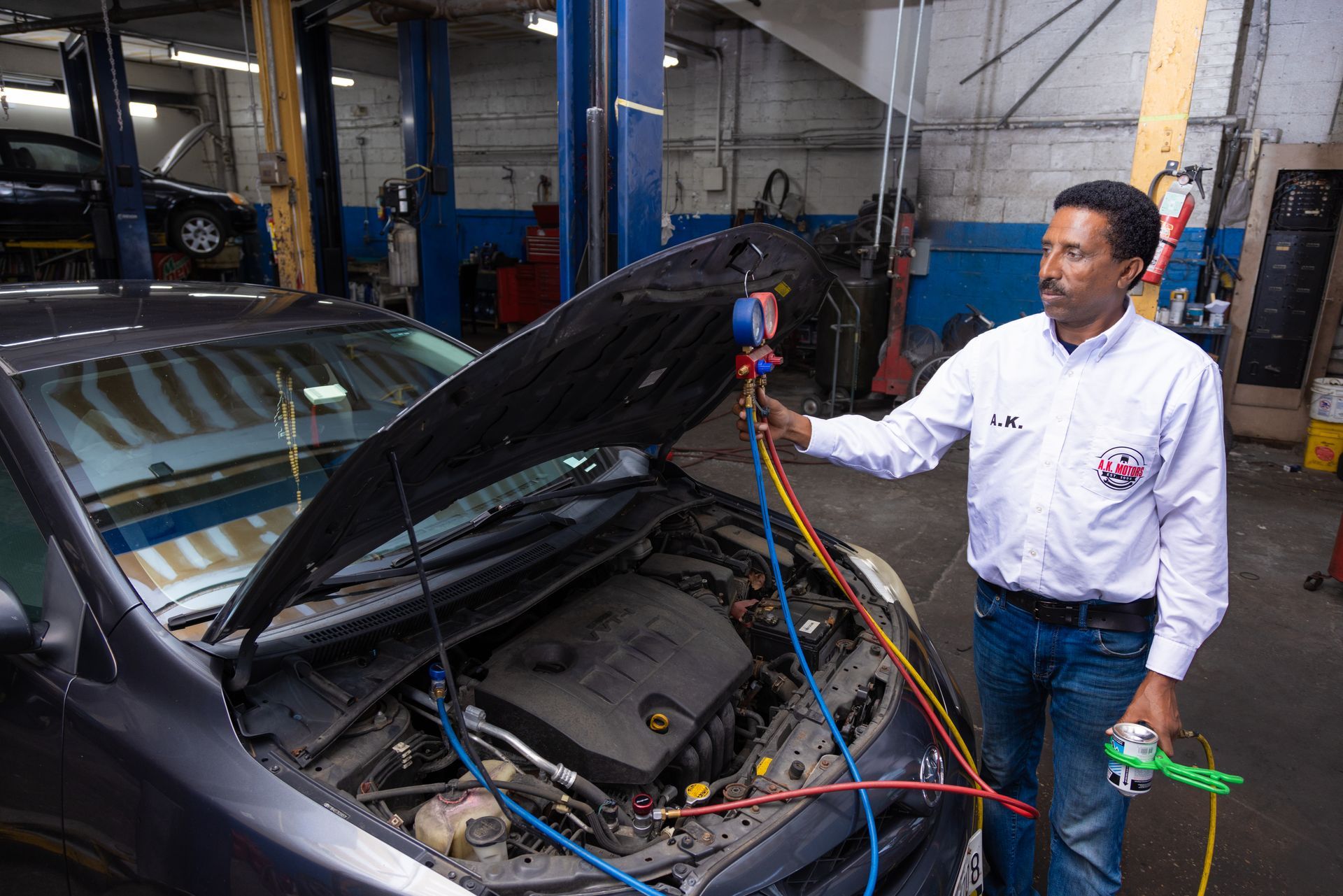 Mechanic inspecting a car's engine with gauges in a repair shop. The hood is open.