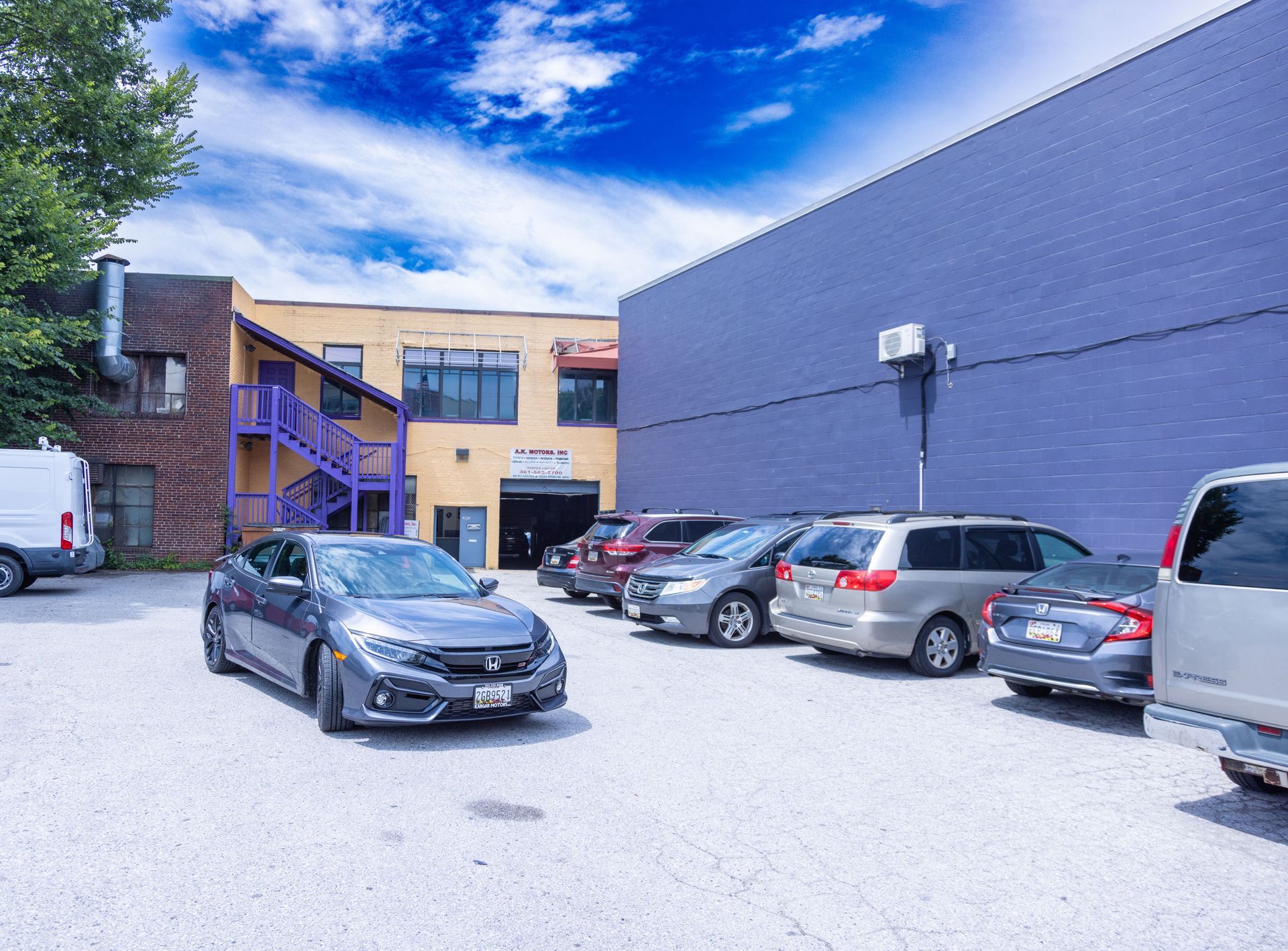 Cars parked in front of a blue and tan commercial building under a bright blue sky.