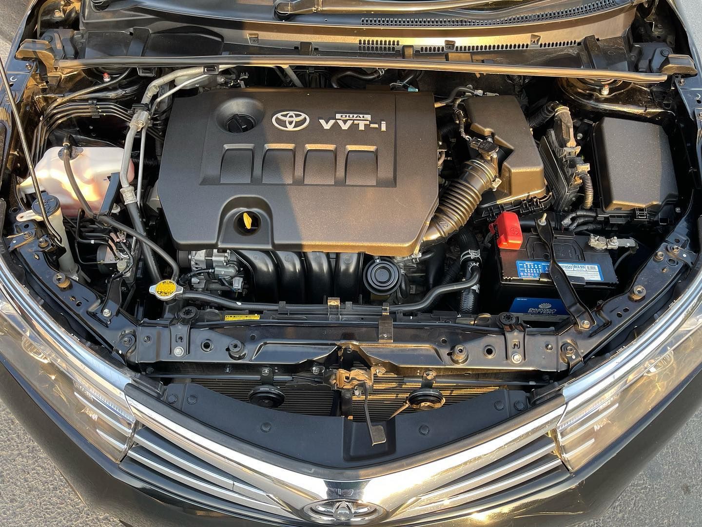 Black Toyota Corolla engine bay, showing engine components and VVT-i branding.