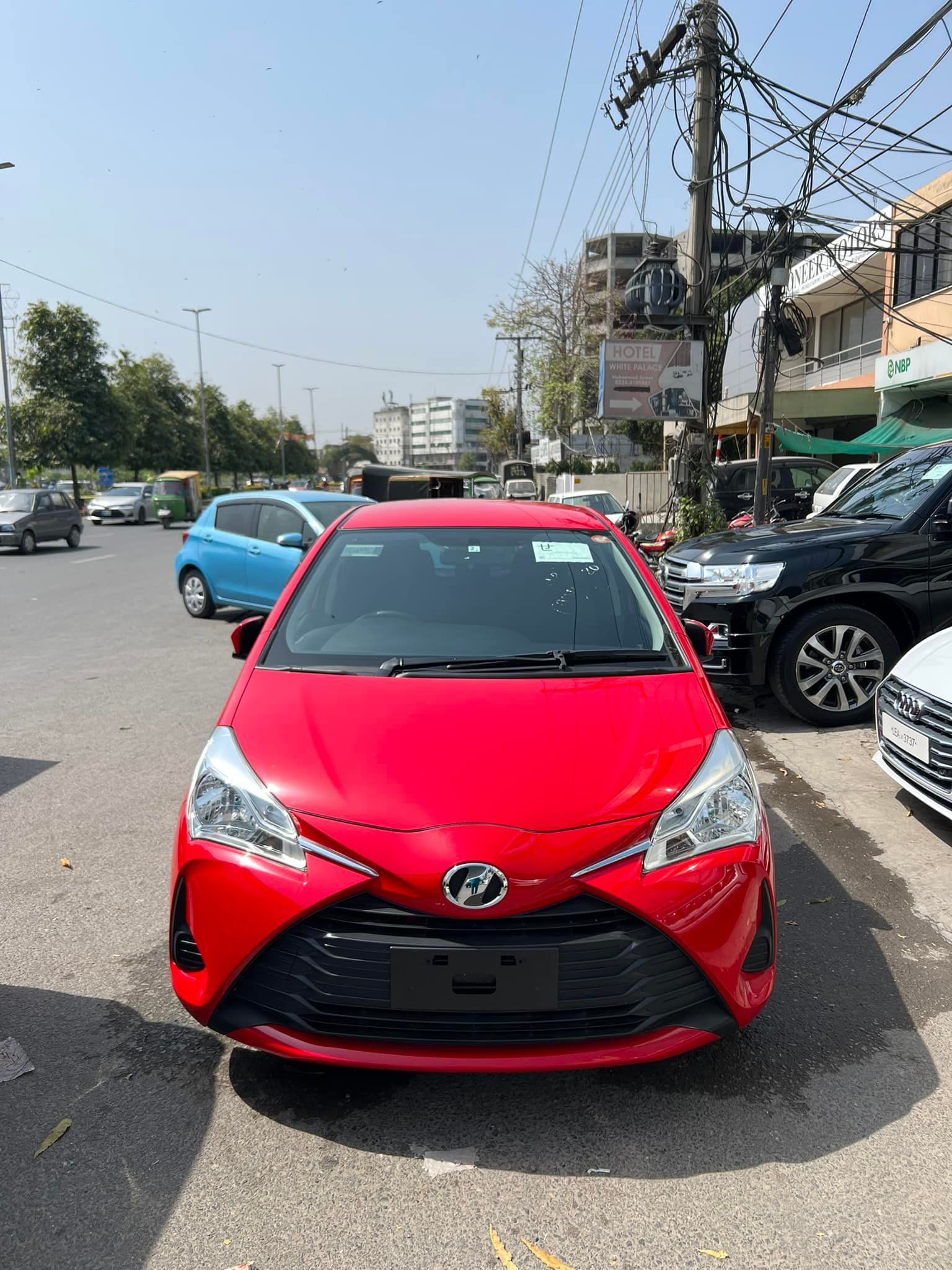 Red Toyota Vitz parked on a street in an urban setting.