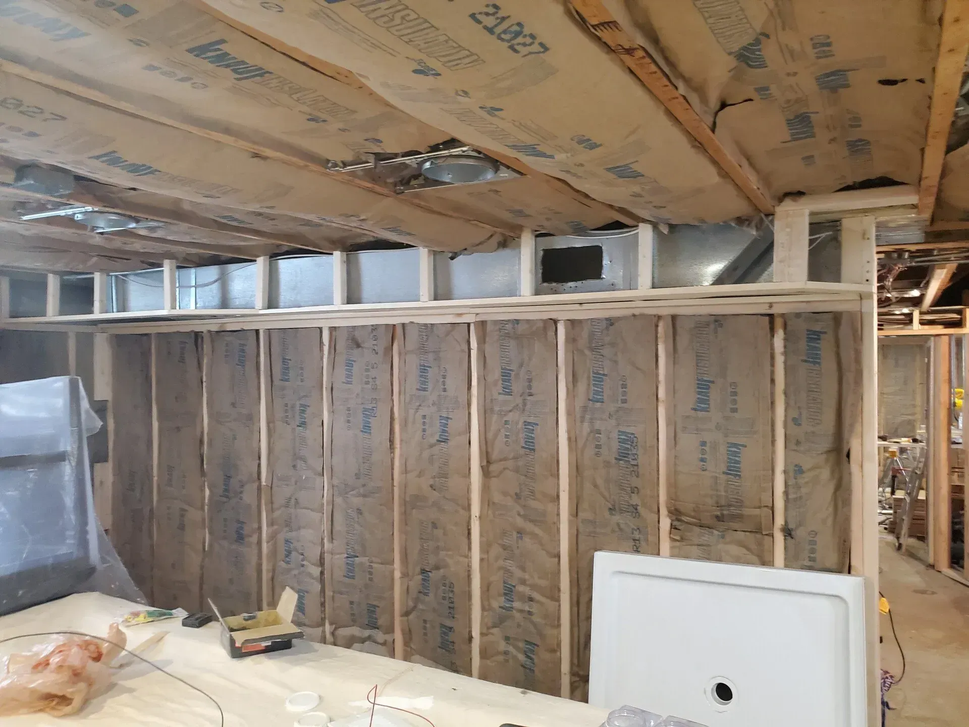 Wood-framed walls with insulation, ductwork, and exposed ceiling joists. A shower base sits nearby.