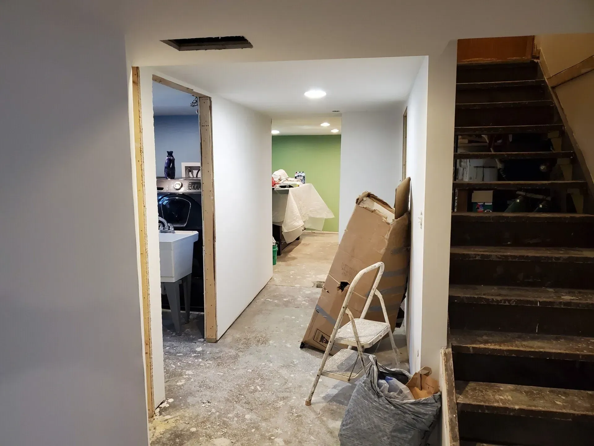 Interior view of a basement hallway under construction, with open doorways, stairs, and construction materials.