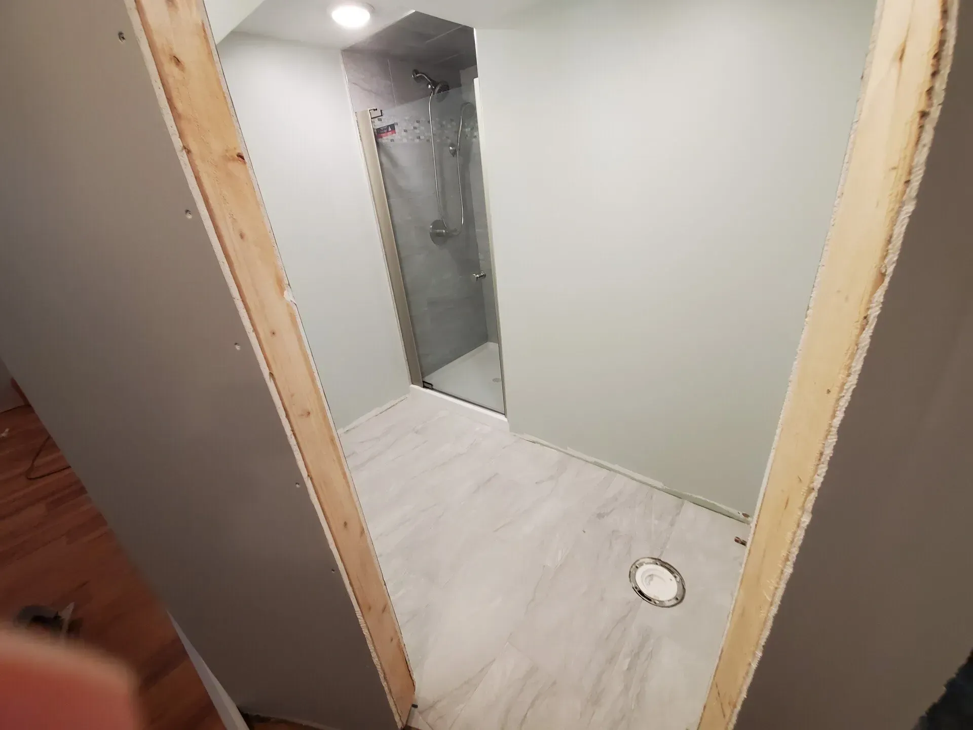 Bathroom with a shower stall, light gray walls, and white flooring viewed from the doorway.