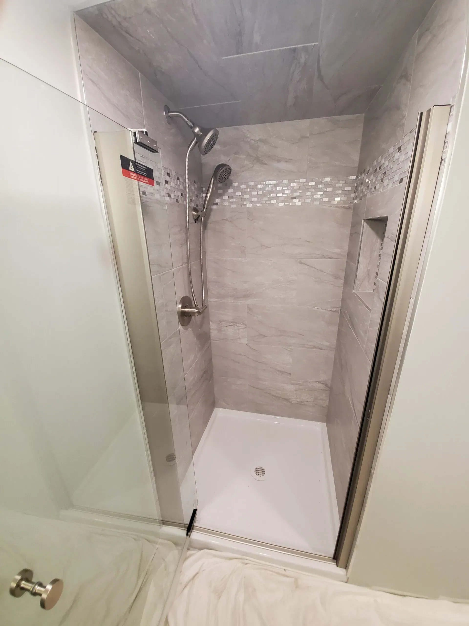 A walk-in shower with gray tile, glass doors, and a white shower pan.