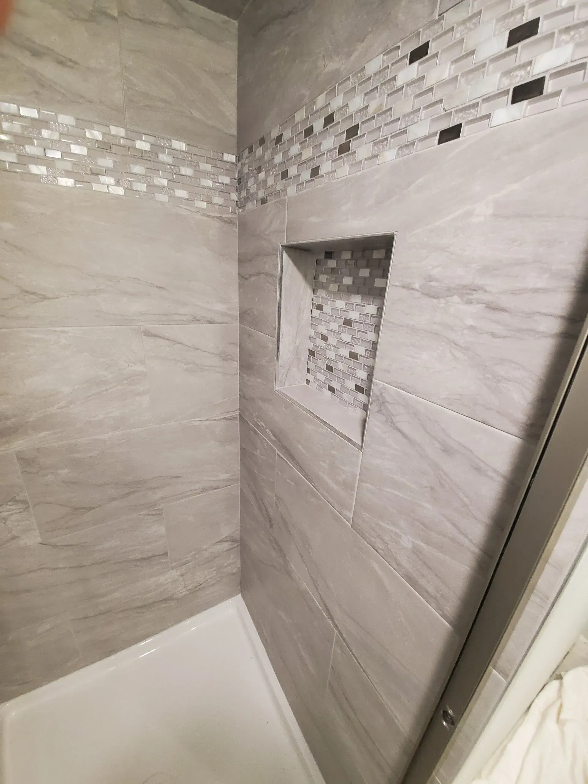 Gray tiled shower with a decorative mosaic tile strip and recessed niche.