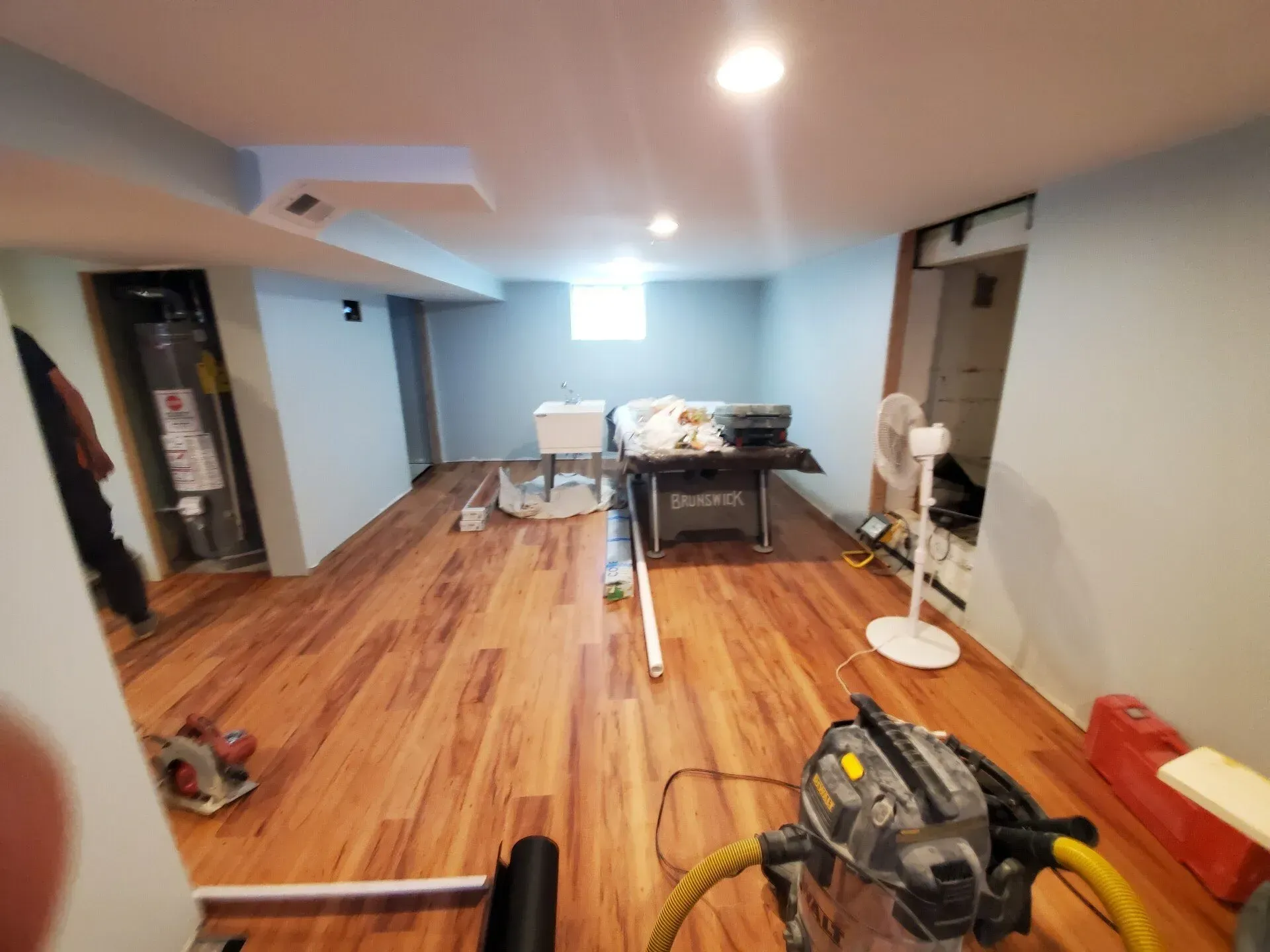 Basement with new wood flooring, tools, and a water heater, likely under construction.