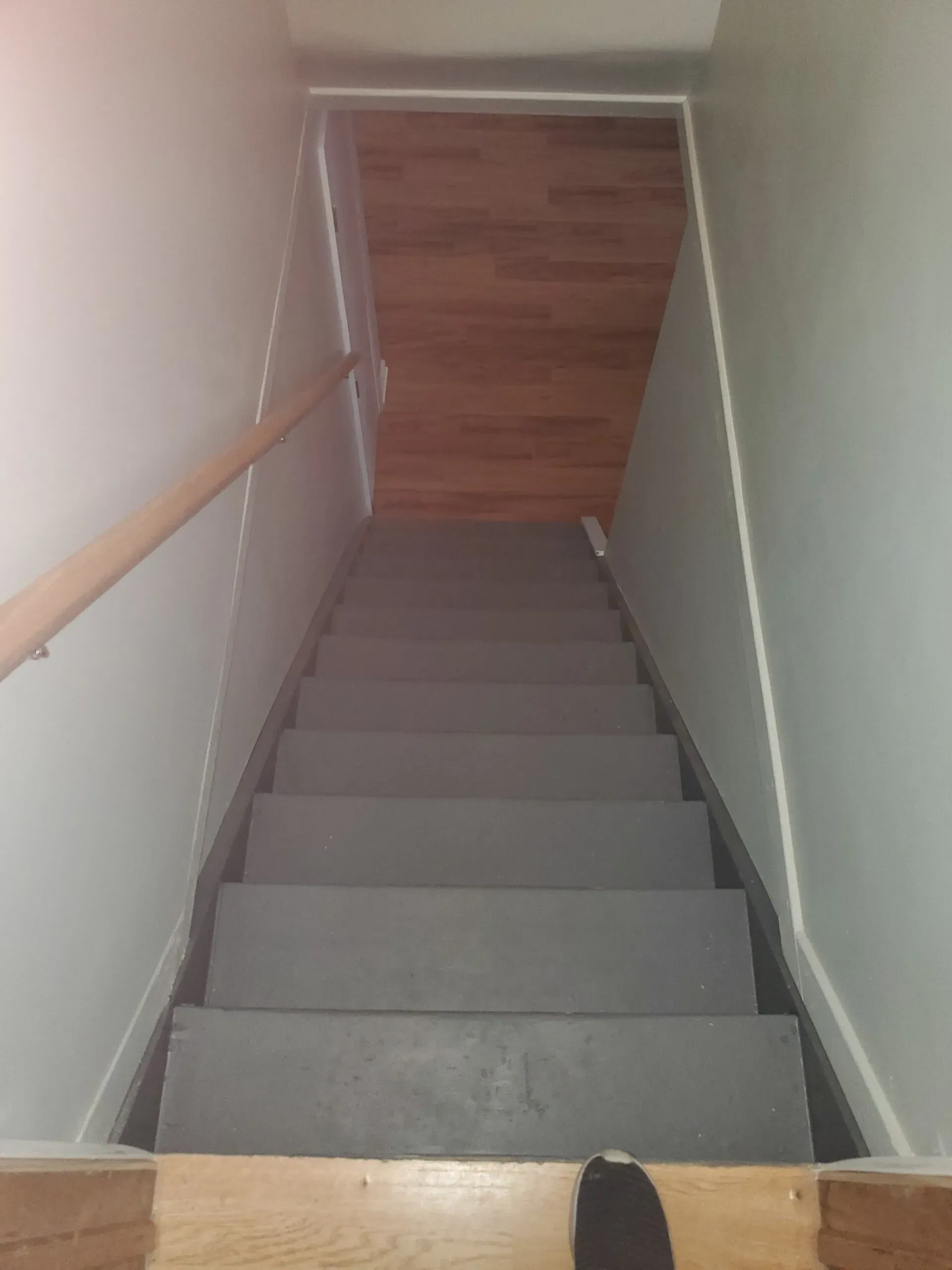 Staircase descending from a wooden floor landing, painted gray, with a wooden handrail.