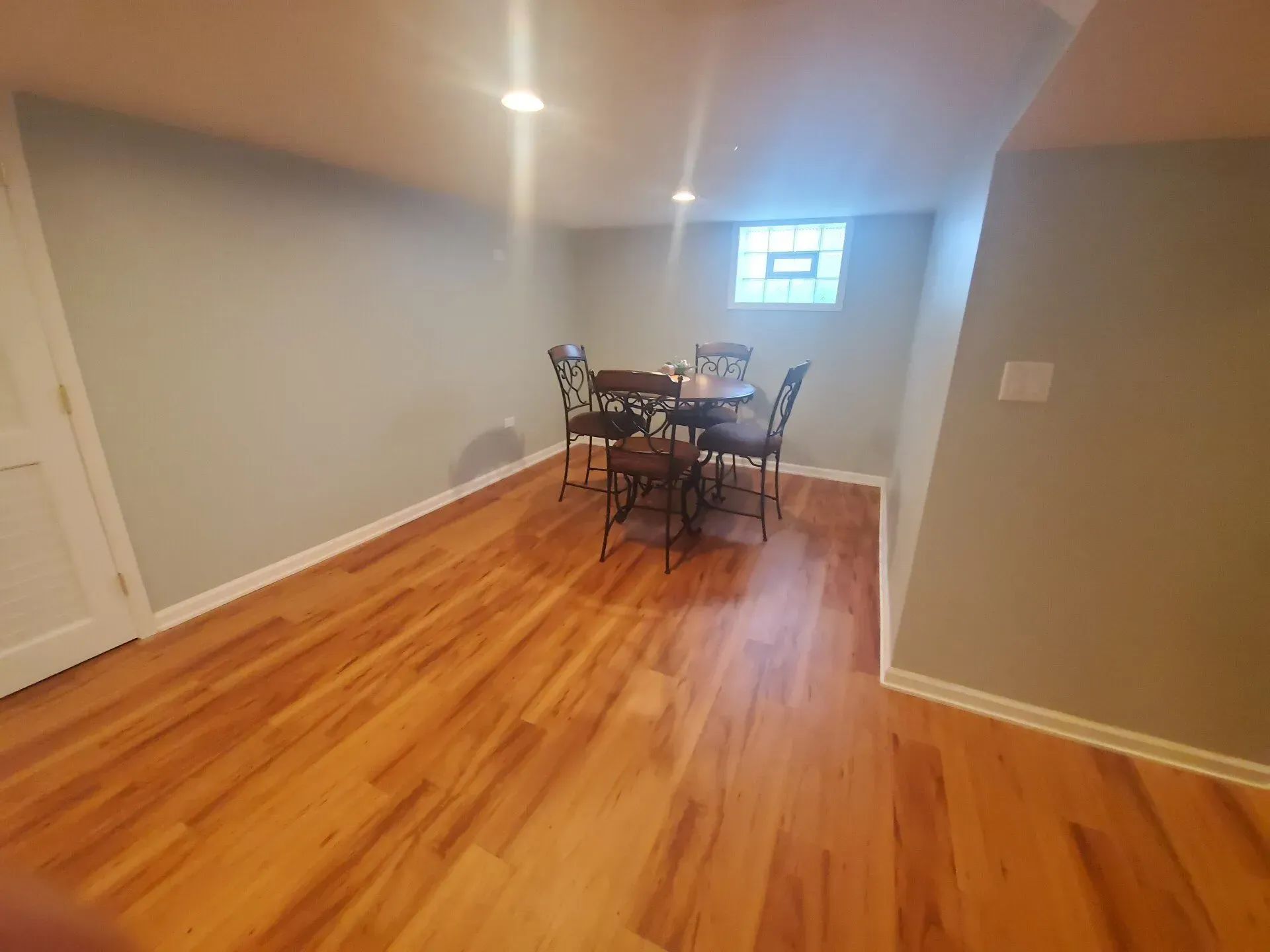 Basement with wood floor, gray walls, table, chairs, and small window.