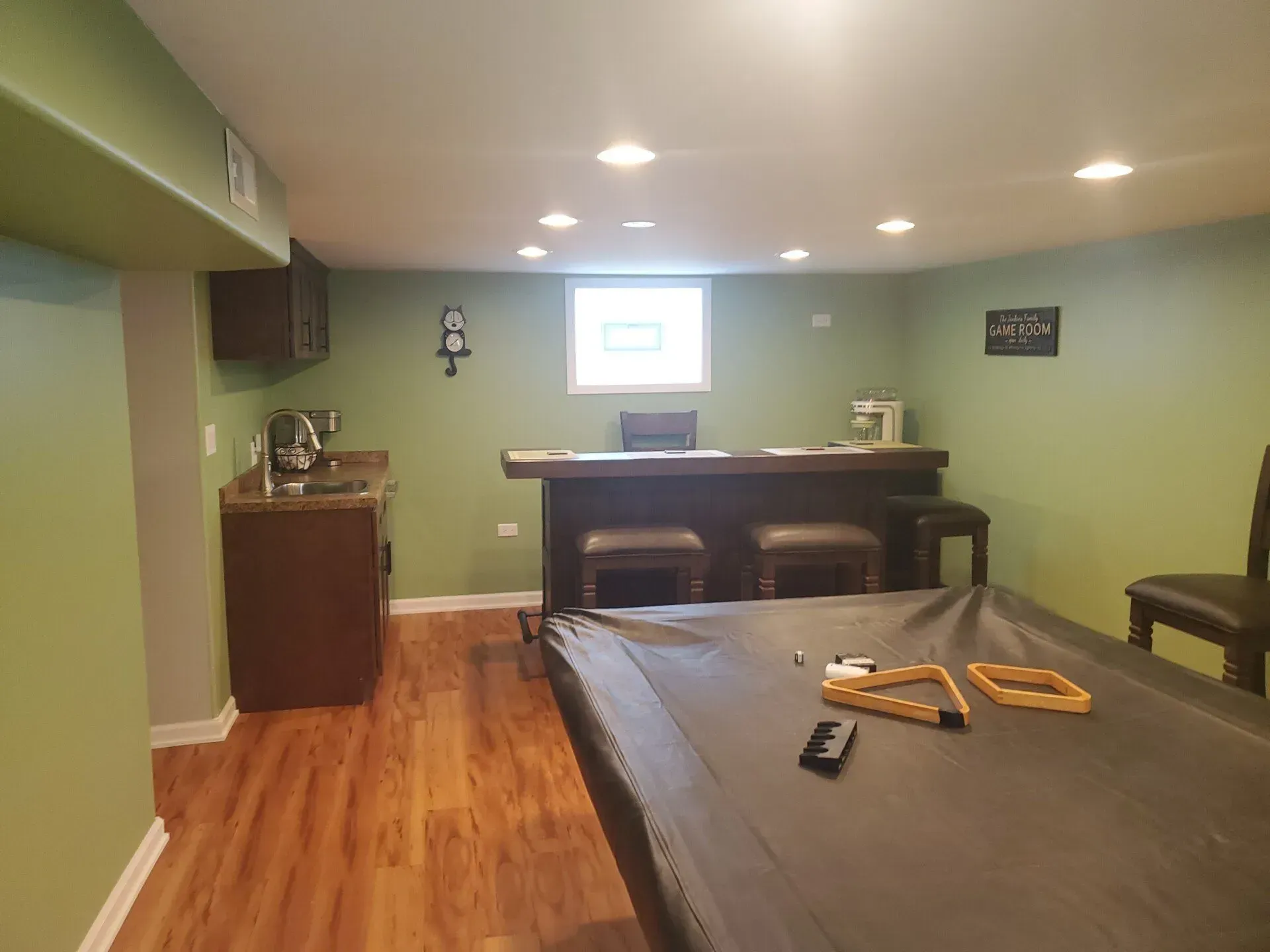 Basement with bar, pool table, and small sink area; green walls, brown flooring.