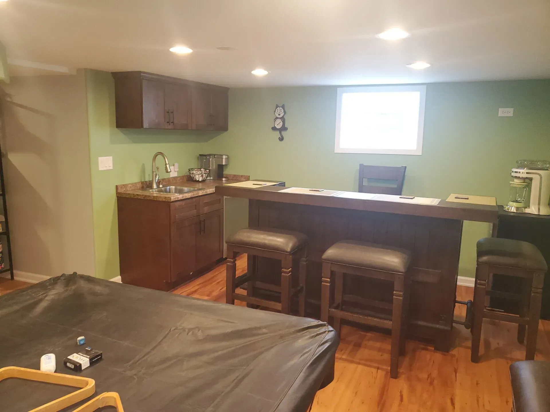 Basement bar with dark wood cabinets, stools, and green walls. 